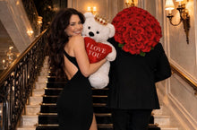 Load image into Gallery viewer, Man and woman in formal attire holding a teddy bear and bouquet of red roses in an elegant staircase setting.
