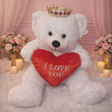 Load and play video in Gallery viewer, Large white teddy bear, with black eyes and nose and smile. Teddy bear wears a sparkling red and clear sparkling stones crown on its head. Teddy bear holds a red heart with the words I Love You embroidered on it.
